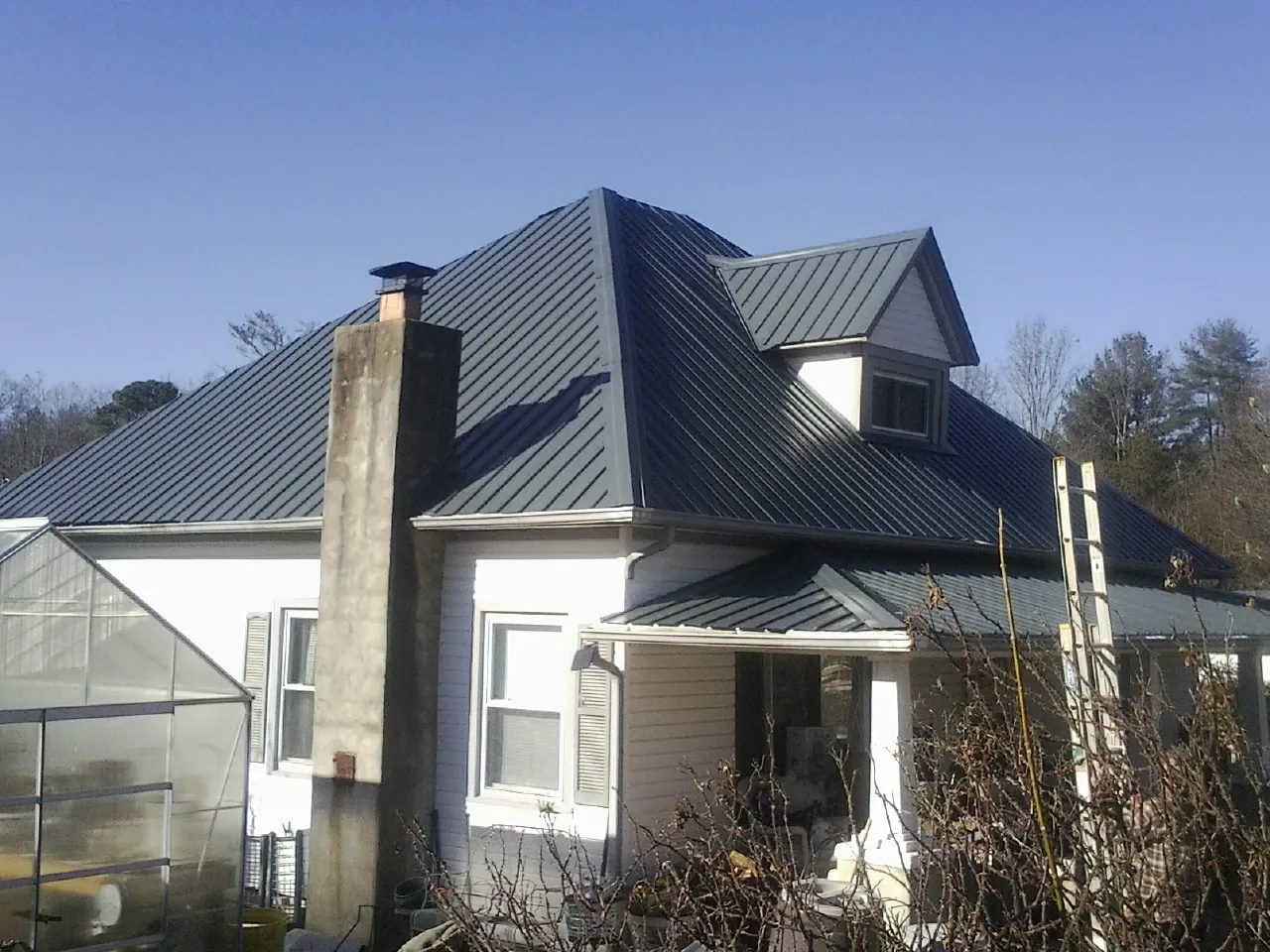Dark blue standing seam metal roof on a white farmhouse with dormer — Slate & Tile Roof Repair by Roofing Brothers in Snook