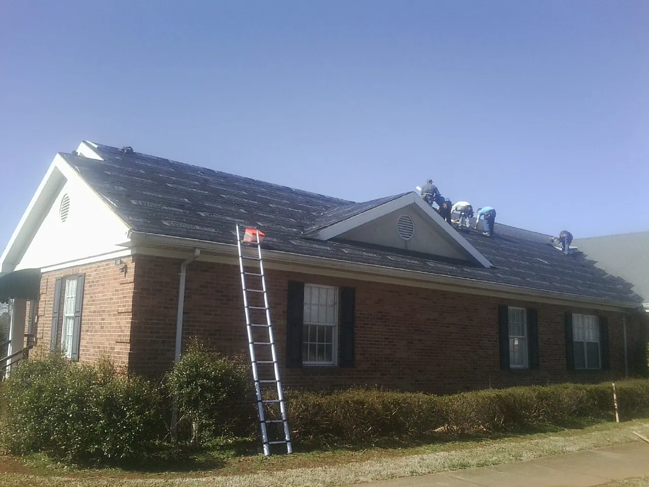 Crew tearing shingles off a brick ranch roof with a ladder set — Emergency Roof Repair work by our crew in Snook