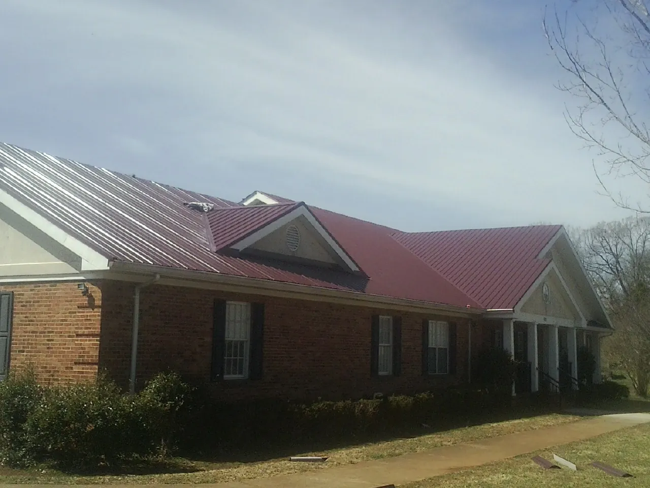Red metal roof with gabled entries on a long brick building, from a Hail Damage Roof Repair job in Snook