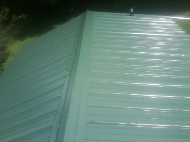 New green metal panels meeting at the ridge of a roof — Flat Roof Repair work by our crew in Snook