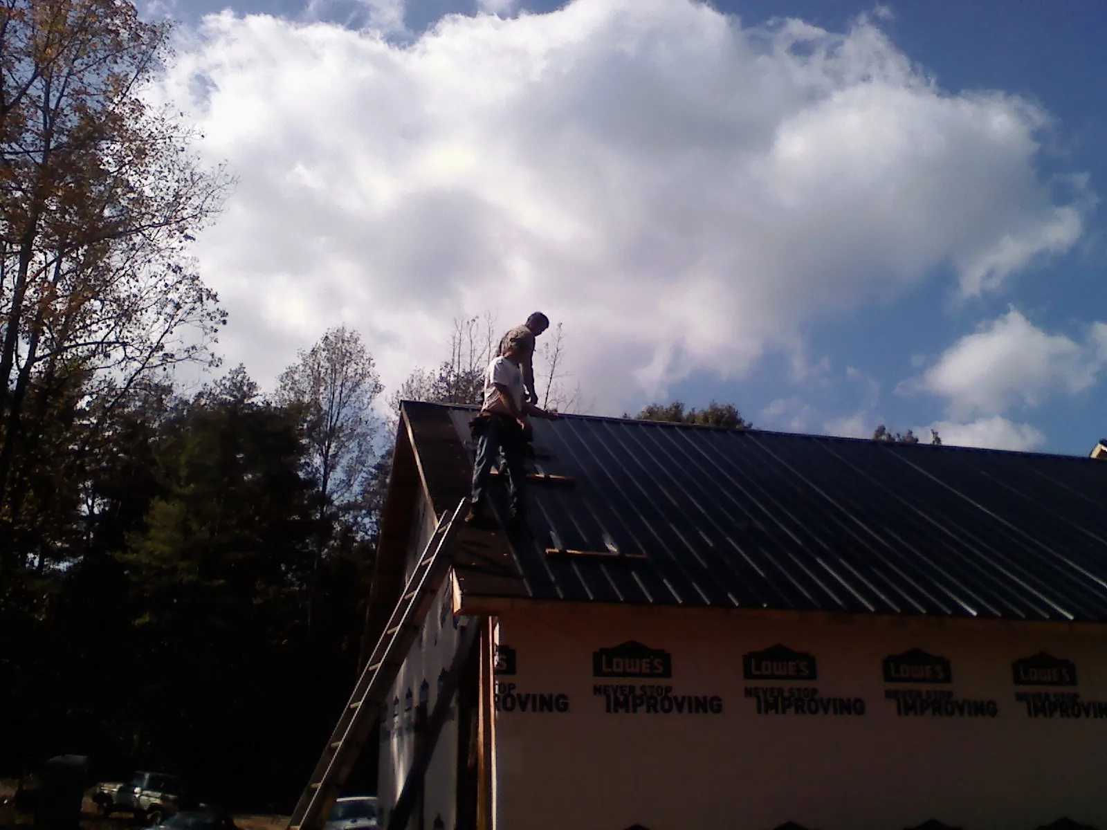Roofer fastening dark metal panels high against a cloudy sky, from a Roof Inspection job in Snook